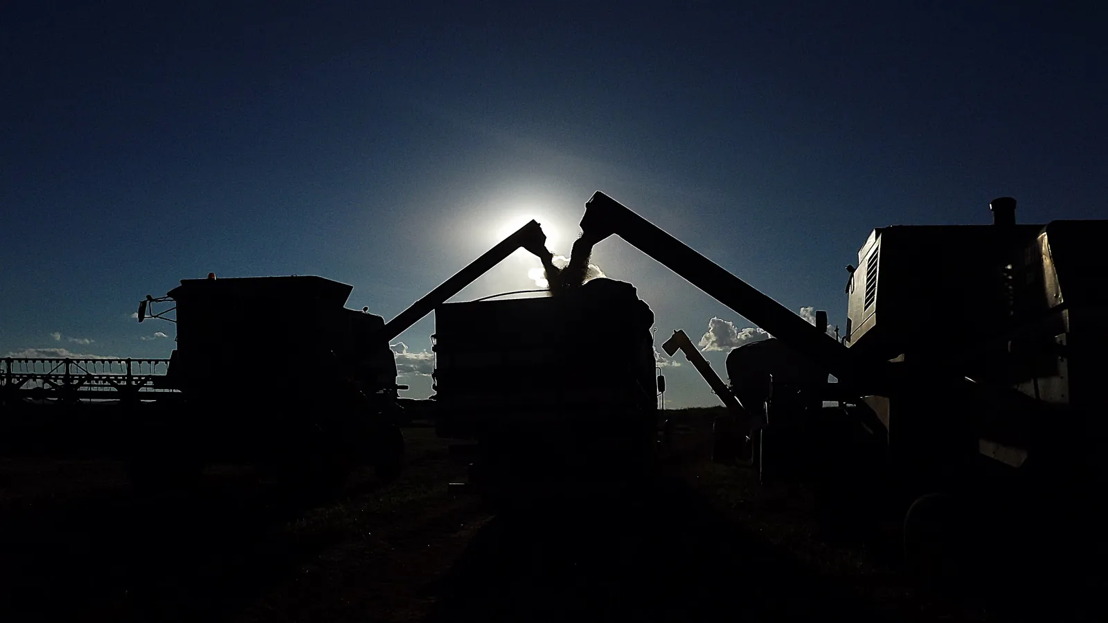 Colheitadeiras descarregam soja em caminhão contra o sol, em Goiatuba