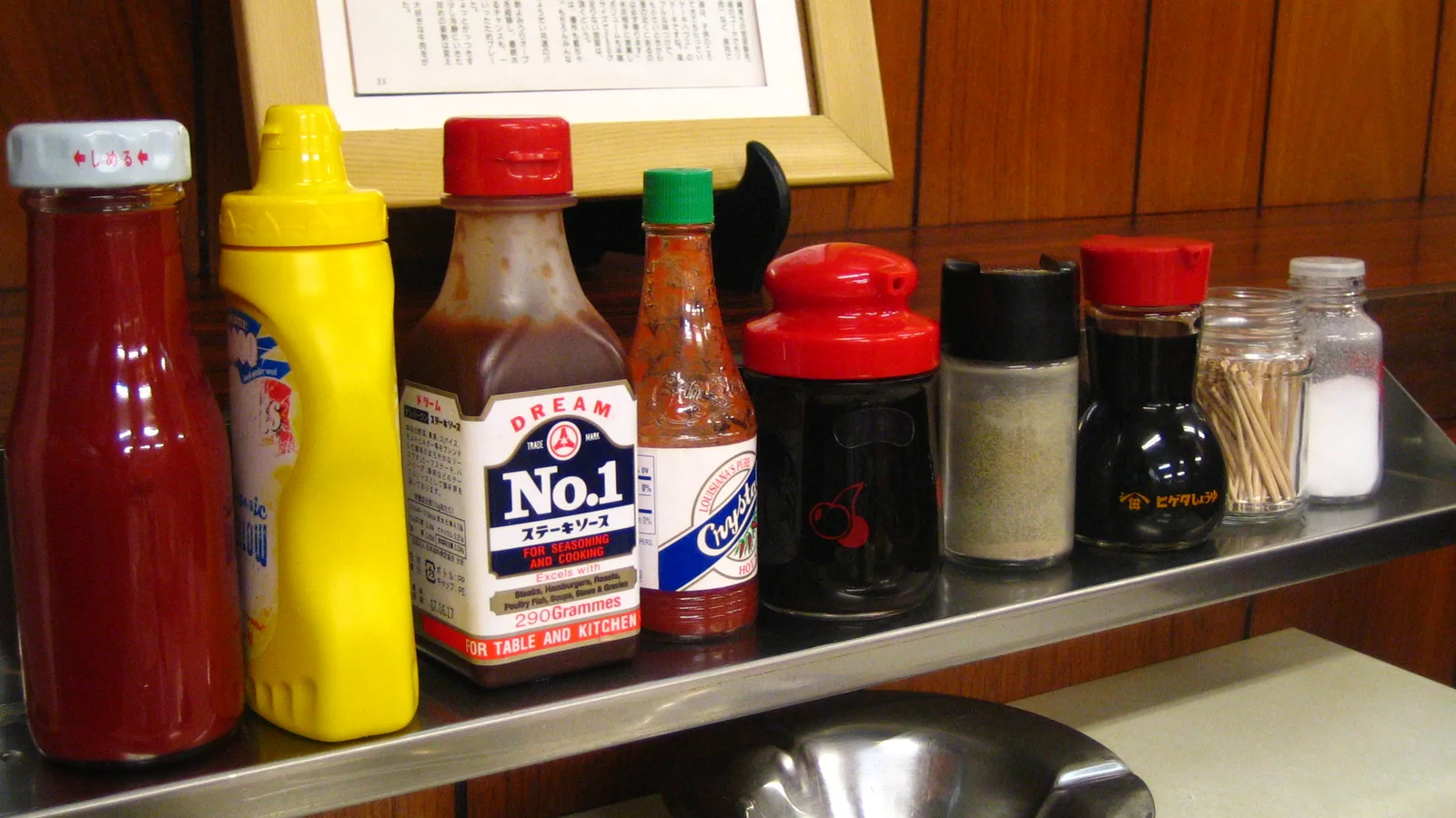 Bisnagas de ketchup, mostarda e outros molhos enfileiradas no balcão de um restaurante