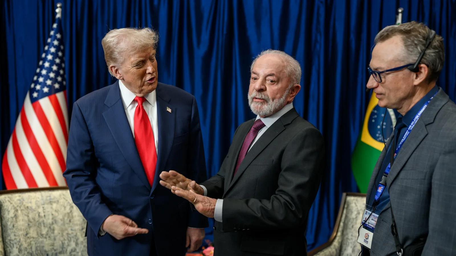 Trump e Lula conversam de pé, com as bandeiras dos Estados Unidos e do Brasil ao fundo