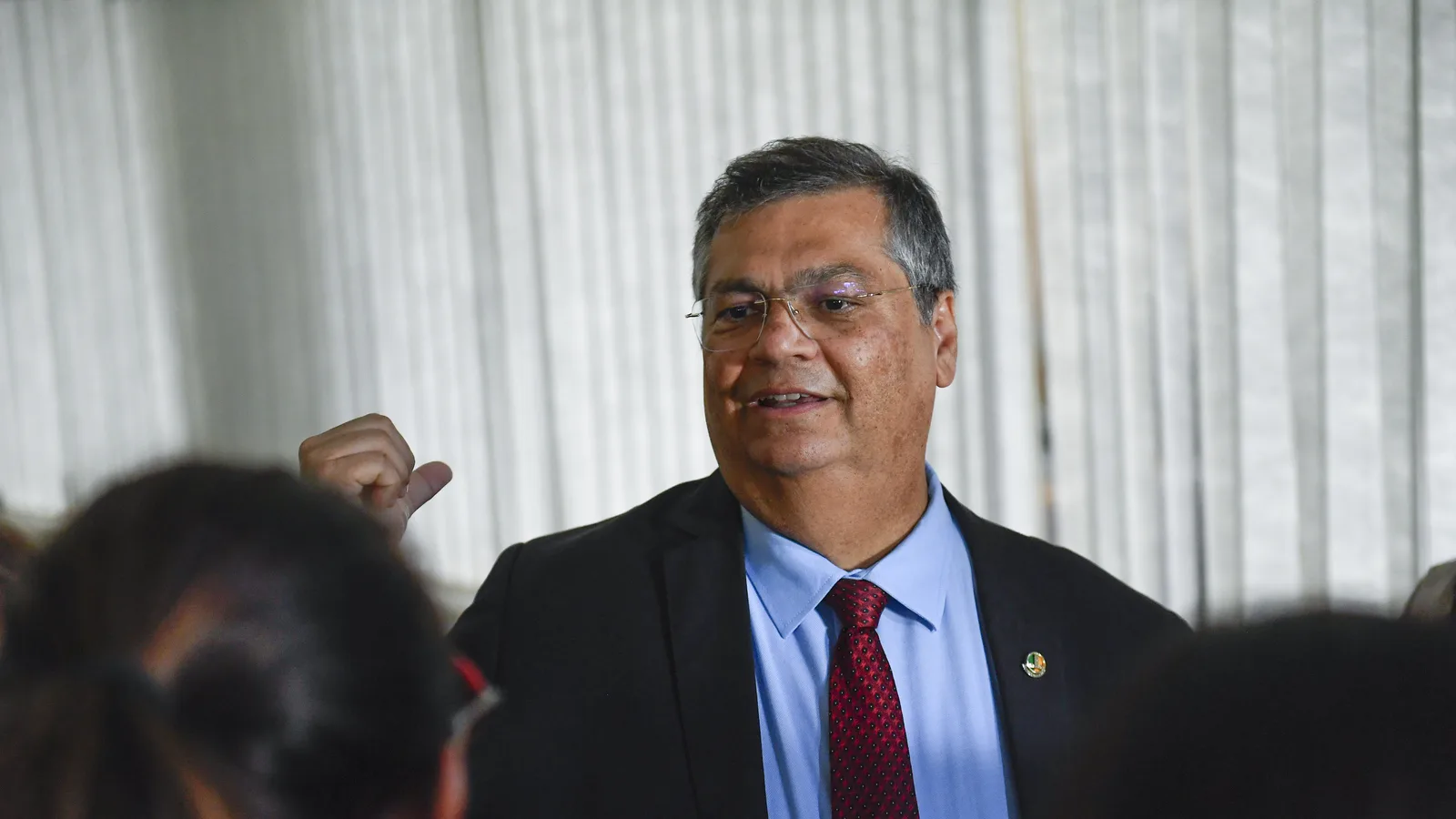Flávio Dino de terno e gravata vermelha, falando a jornalistas