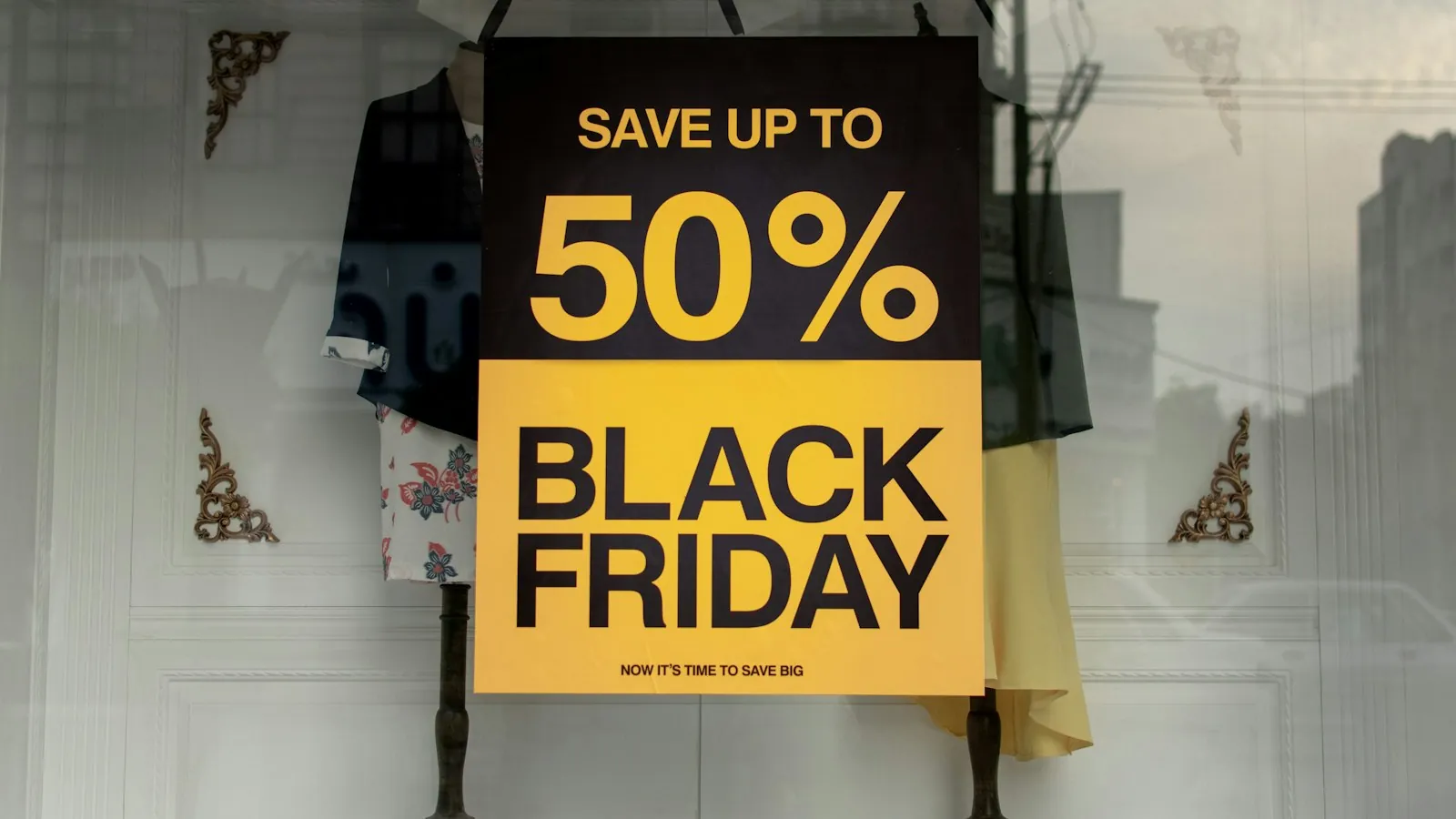 Cartaz amarelo e preto de Black Friday anuncia até 50% de desconto na vitrine de uma loja de roupas